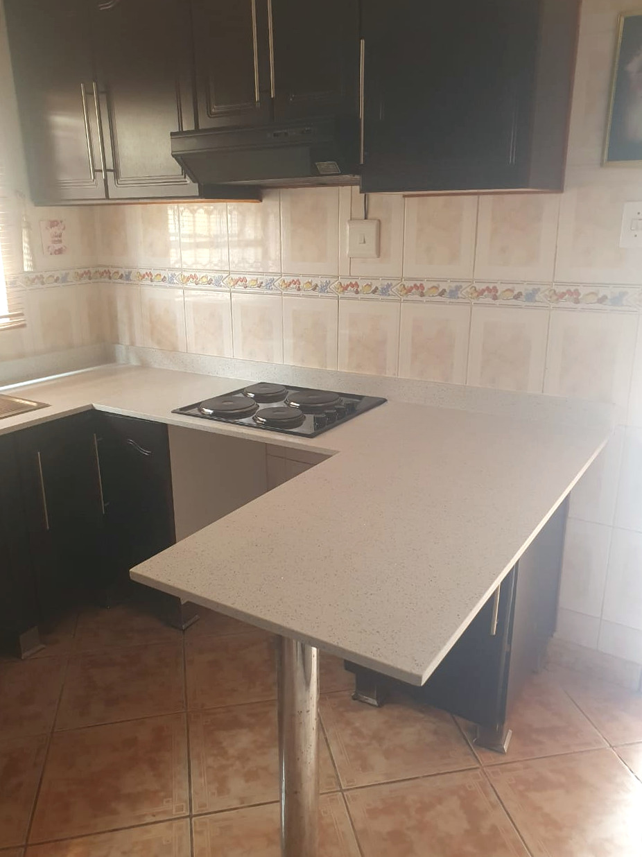 Light quartz L-shaped kitchen top with a built-in hob and a quartz breakfast bar on a steel leg