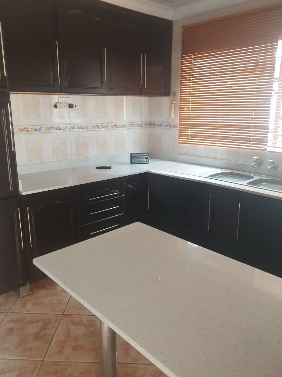 Light quartz kitchen island in front of an L-shaped quartz counter with dark cupboards and the sink under a window