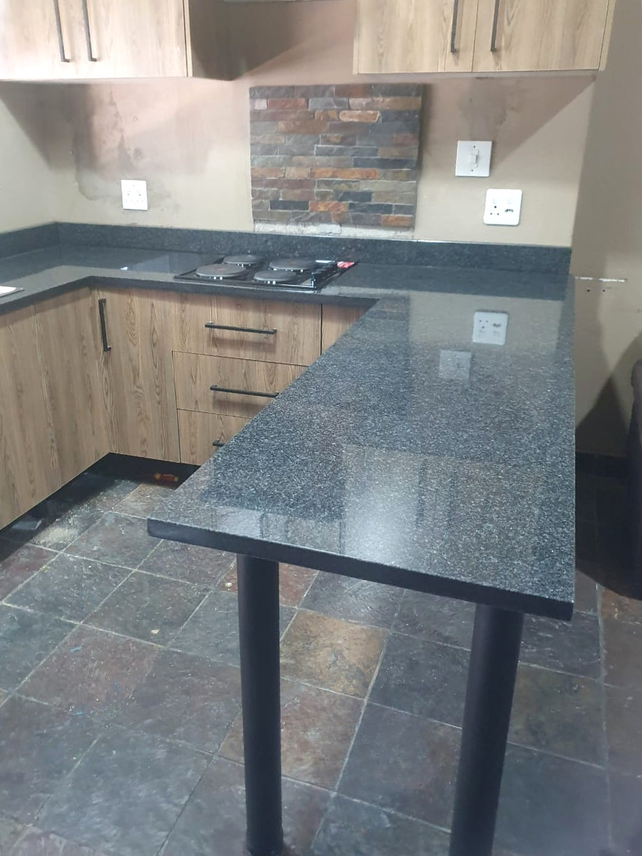 Dark granite breakfast bar on two black steel legs, with the hob run and a stone-effect splashback behind