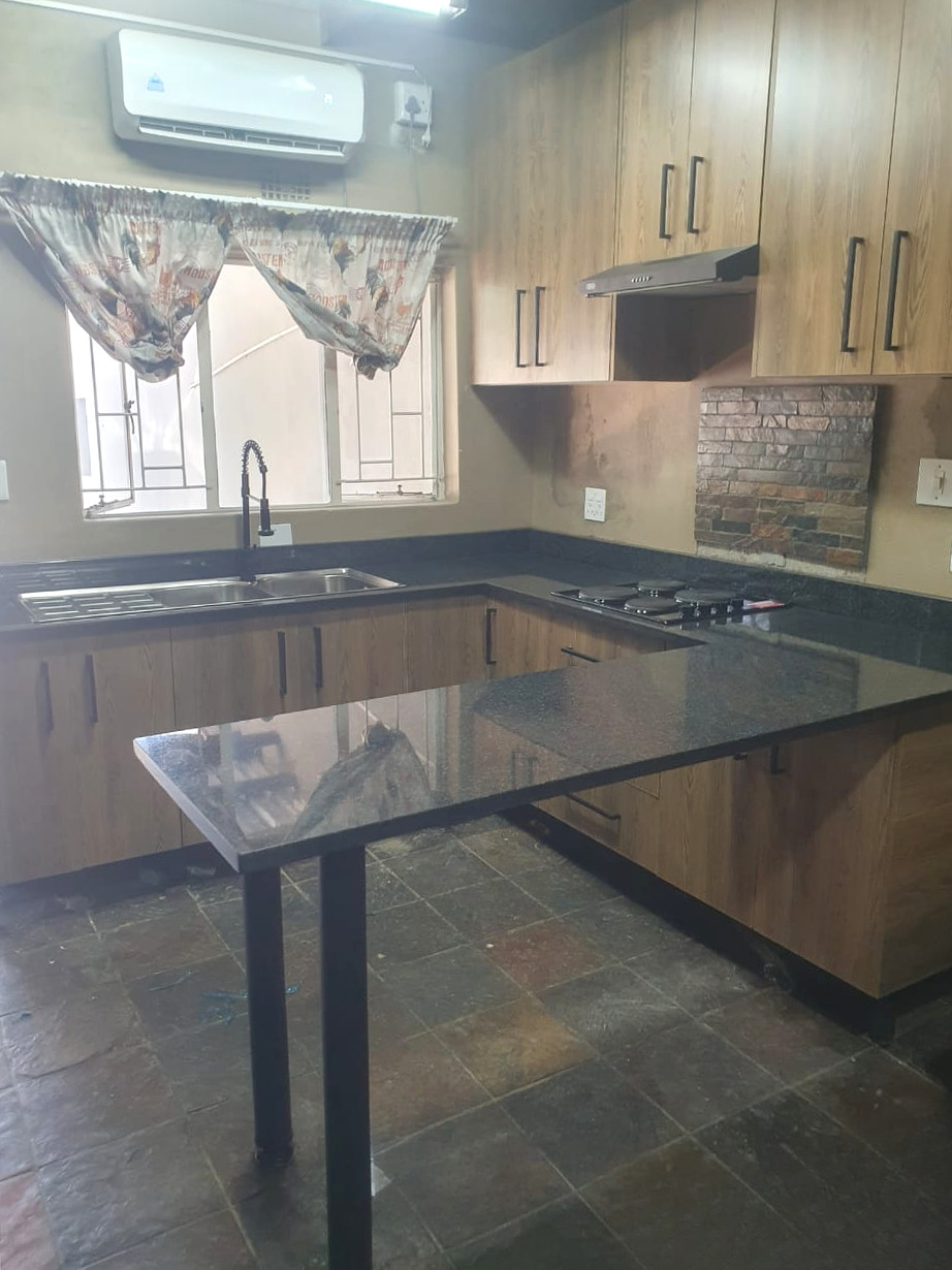 Dark granite L-shaped kitchen top with the sink under a window, the hob in the corner and a granite breakfast bar in front
